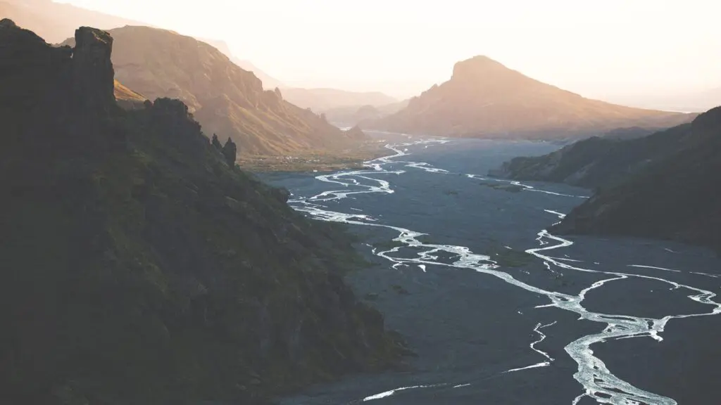 A valley in volcanic location with the sun peaking over the mountains