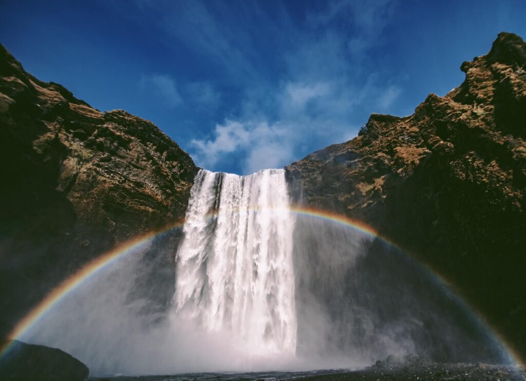 A rainbow crosses Skógafoss waterfall in Iceland - this is one of the best day trips from Reykjavik according to Your Friend in Reykjavik