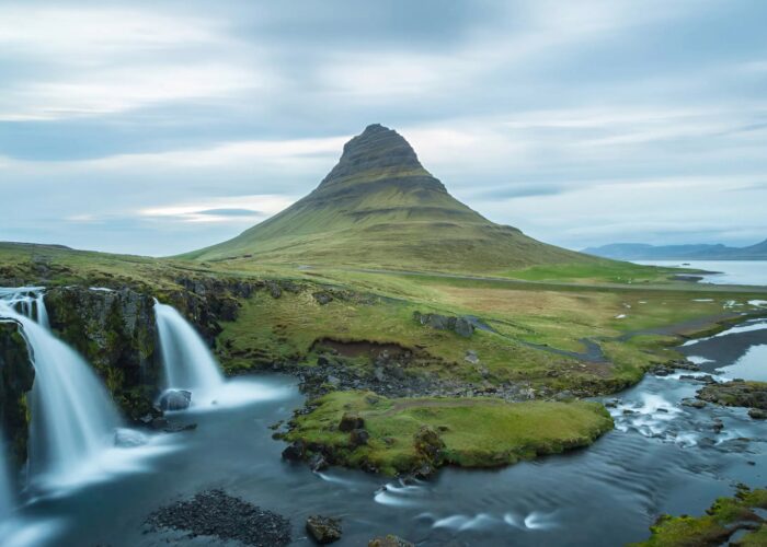 Scenic view of Kirkjufell mountain and waterfall on Snæfellsnes Peninsula, Iceland, with lush green landscape and calm waters, highlighting popular travel destination from Reykjavik.