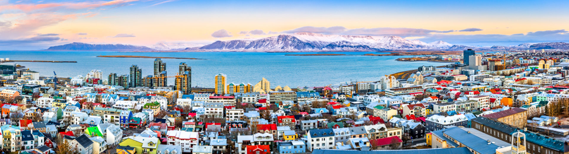 Aerial panorama of downtown Reykjavik at sunset with colorful houses and snowy mountains in the background