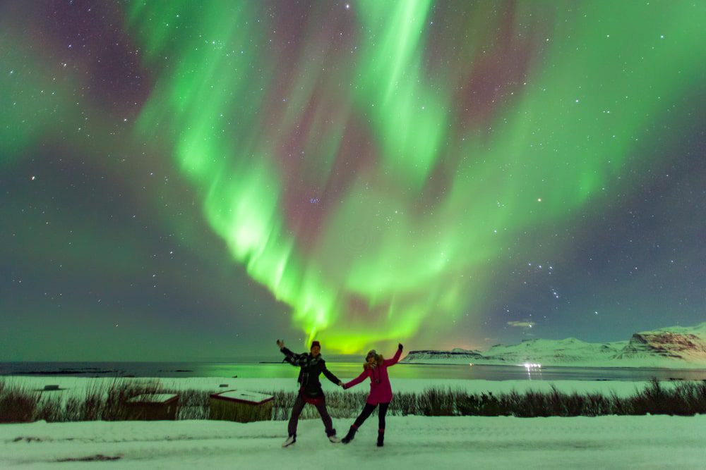 Two travellers striking a pose with northern lights in the background