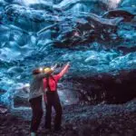 Two people standing in a cave of ice pointing up