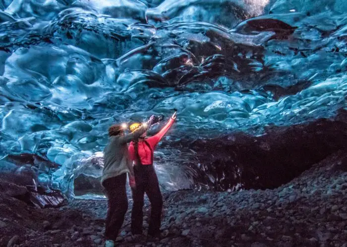 Two people standing in a cave of ice pointing up