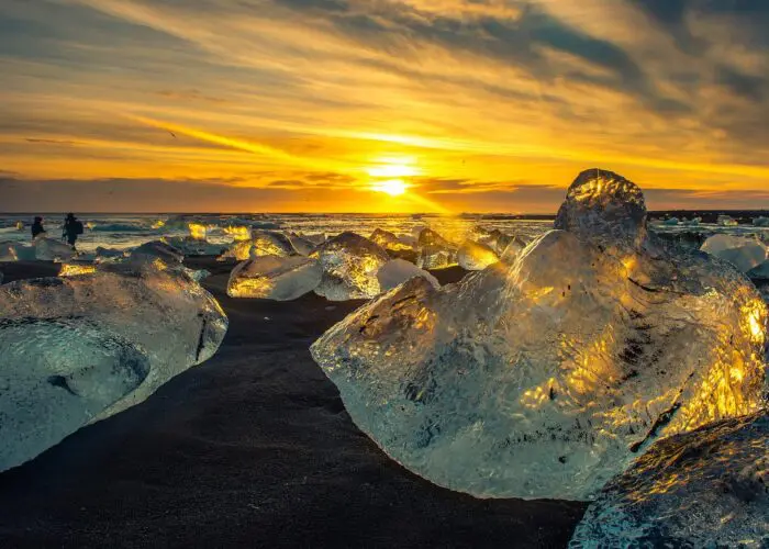 Large chunks of ice on a black beach at sunset