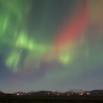 Red and green northern lights above a town