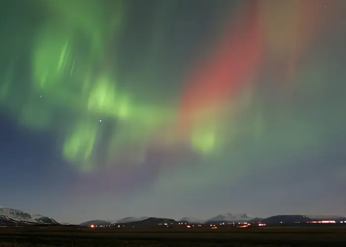 Red and green northern lights above a town