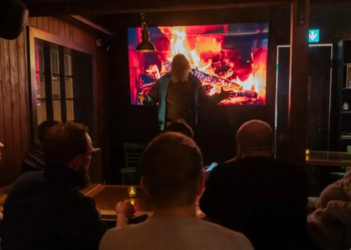 A man with long white hair giving a presentation, with an engaged audience captivated by the magic of The Icelandic Storyteller’s stories