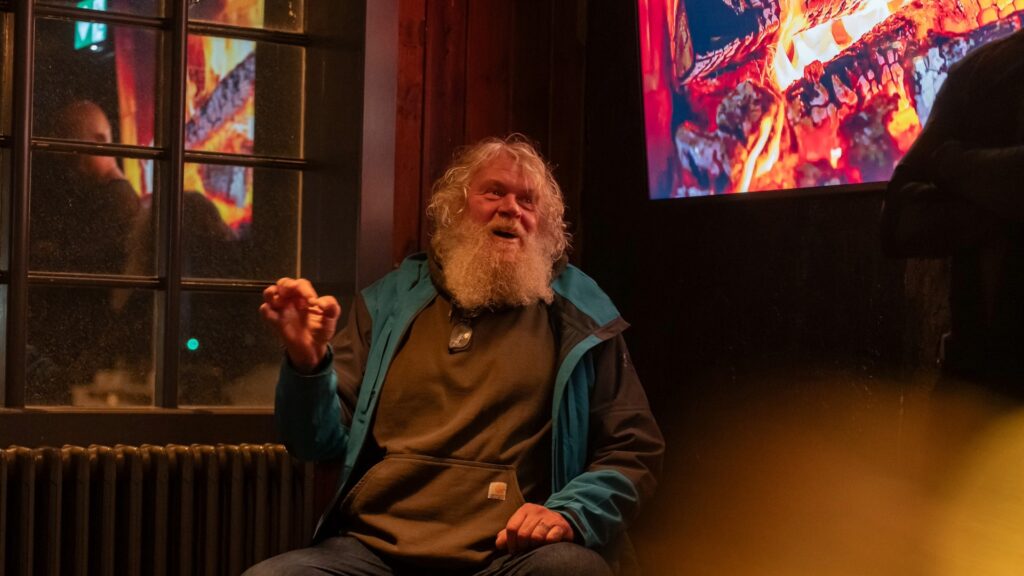 Close-up of the guide with long white hair, his expressive hand raised again, telling tales from the sagas