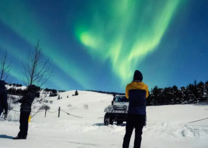 Group of people standing on snow beneath the northern lights