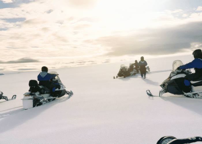 Snowmobiles driving across a glacier under a cloudy yet sunny sky