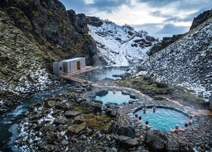 Aerial view of Húsafell Canyon Baths in winter with guests soaking in steaming geothermal pools surrounded by snow-covered lava rock canyon
