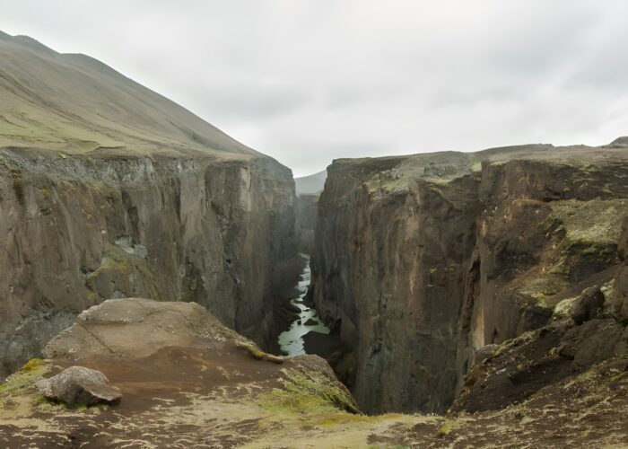 Deep rocky canyon with steep cliffs, a narrow river below, and moss-covered volcanic terrain.